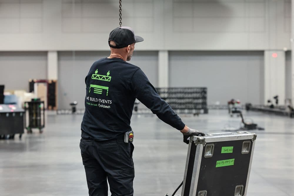 OnPoint crew member in a We Build Events shirt moving a road case across a venue floor