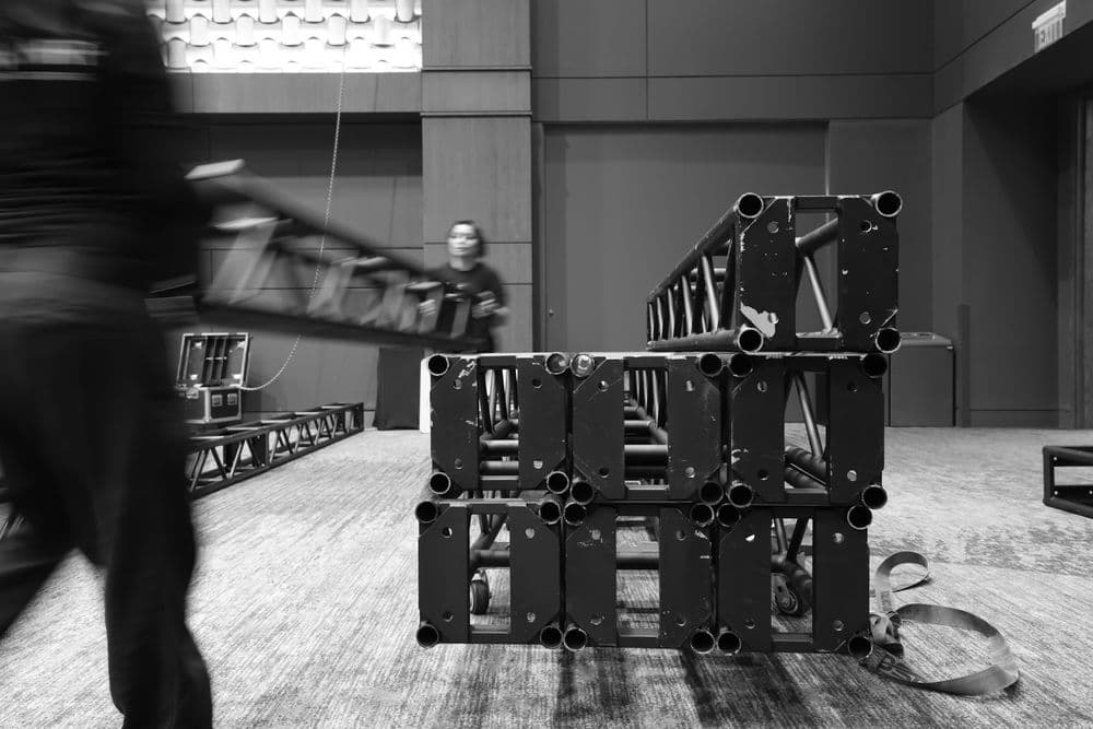Crew member carrying truss past a stacked truss run, black and white
