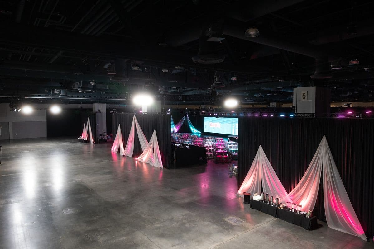 Exhibit hall transformed with drape and pink uplighting