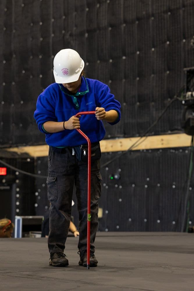 Rigger in a hard hat working a chain pull lift on a venue floor